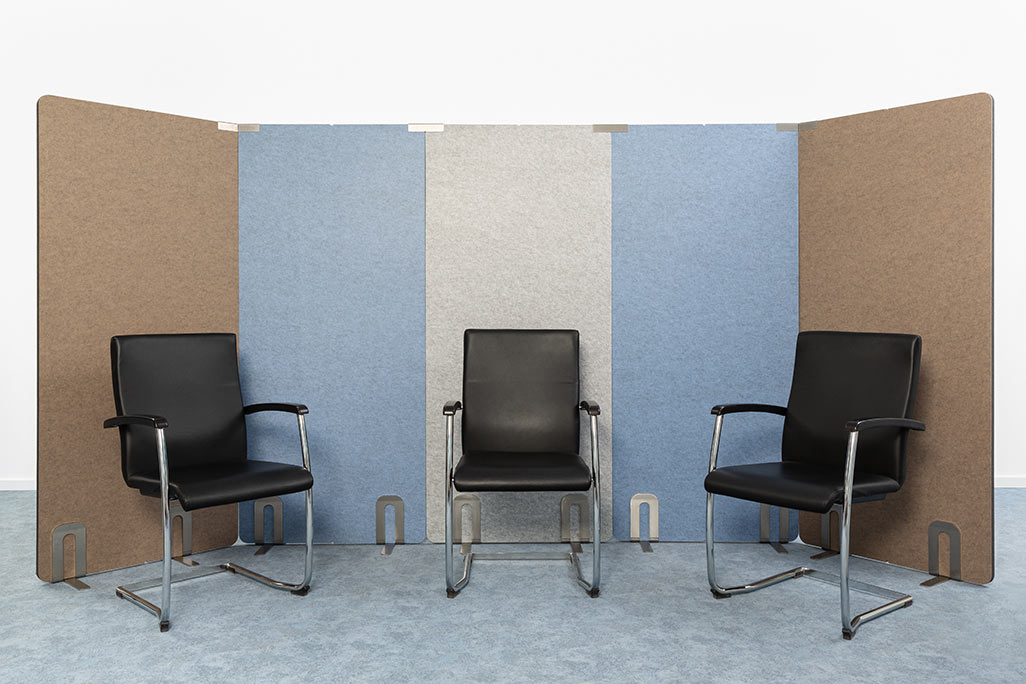 5 partitions from soniflex arranged next to each other in front of a white wall as a U. Several chairs next to each other