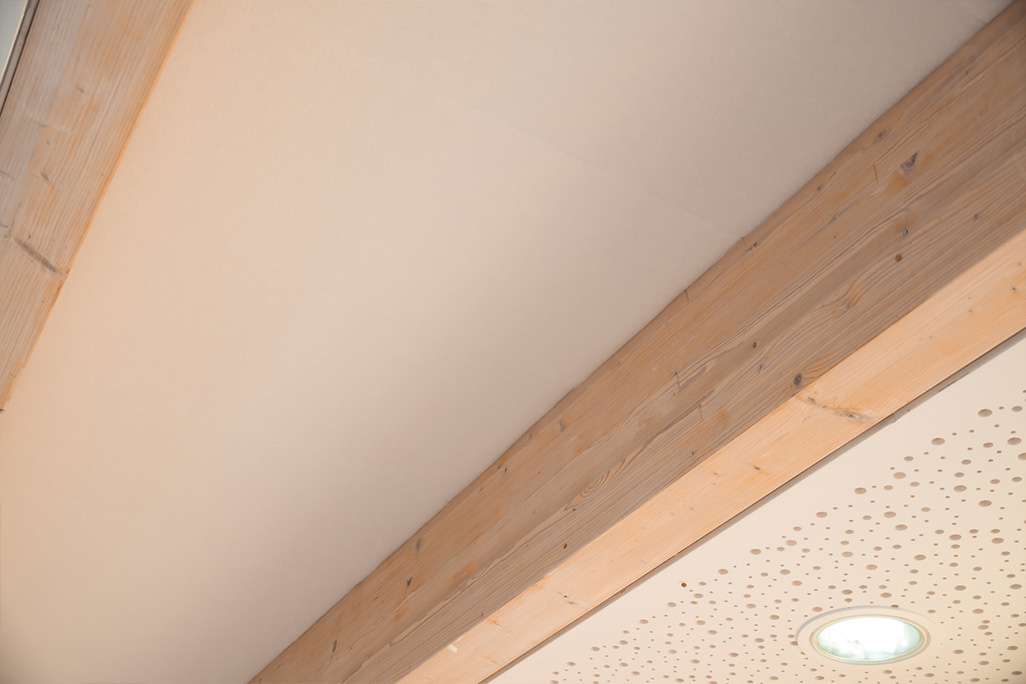 Deckenbalken aus Holz mit weißen Vliesplatten dazwischen