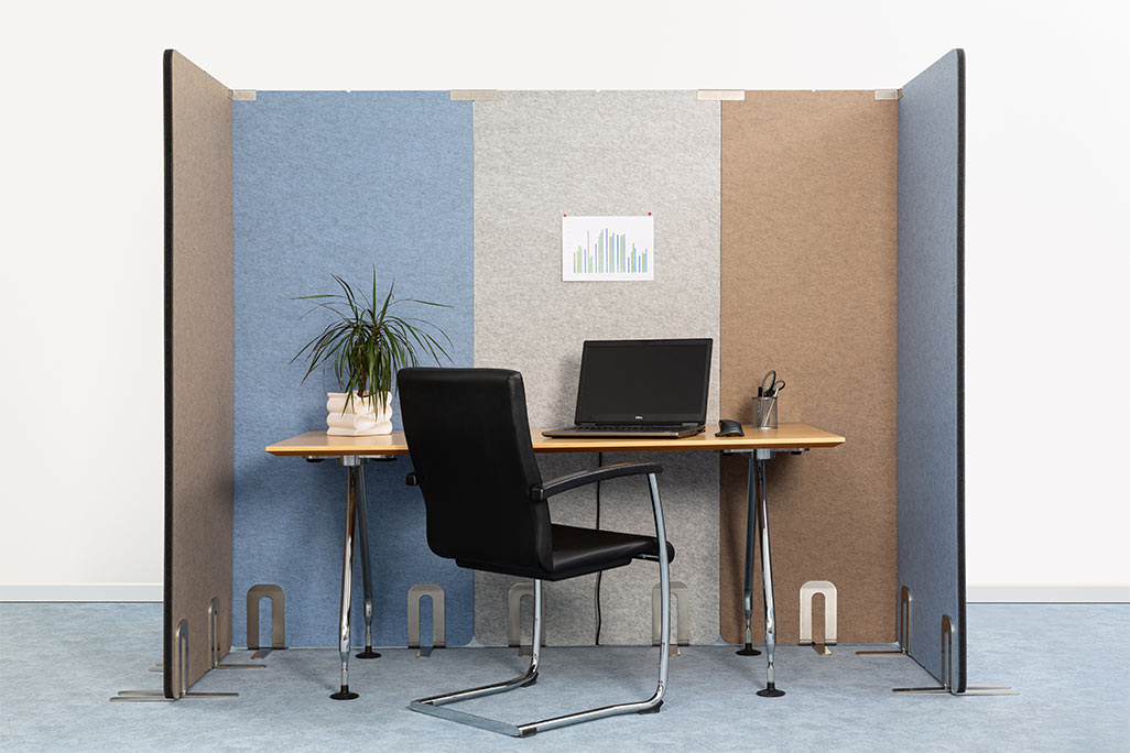 5 partitions from soniflex arranged next to each other in front of a white wall as a U. Inside a desk with laptop and chair