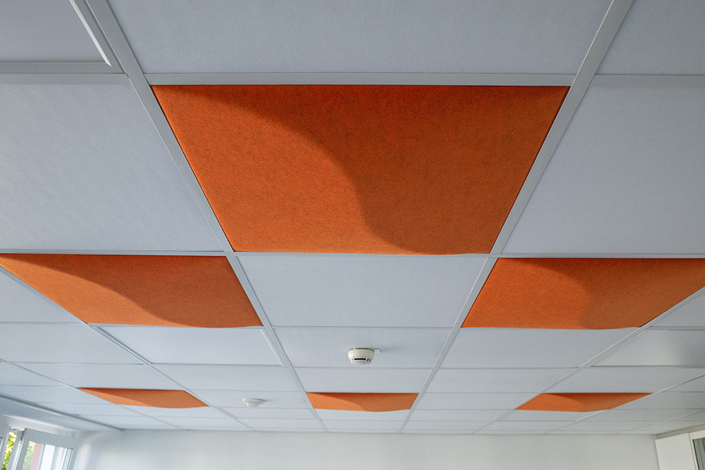 Section of a standard grid ceiling with inlaid soni COMFORT SD acoustic absorbers in white and soni COLOR Design in light orange.