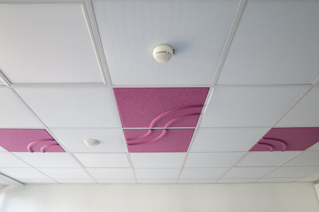 Section of a standard grid ceiling with inlaid soni COMFORT SD acoustic absorbers in white and soni COLOR Design in pink.
