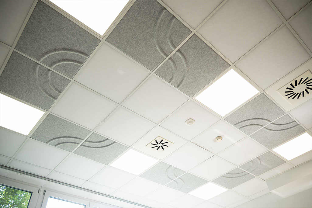 Section of a standard grid ceiling with inlaid soni COMFORT SD acoustic absorbers in white and soni COLOR Design in light gray.