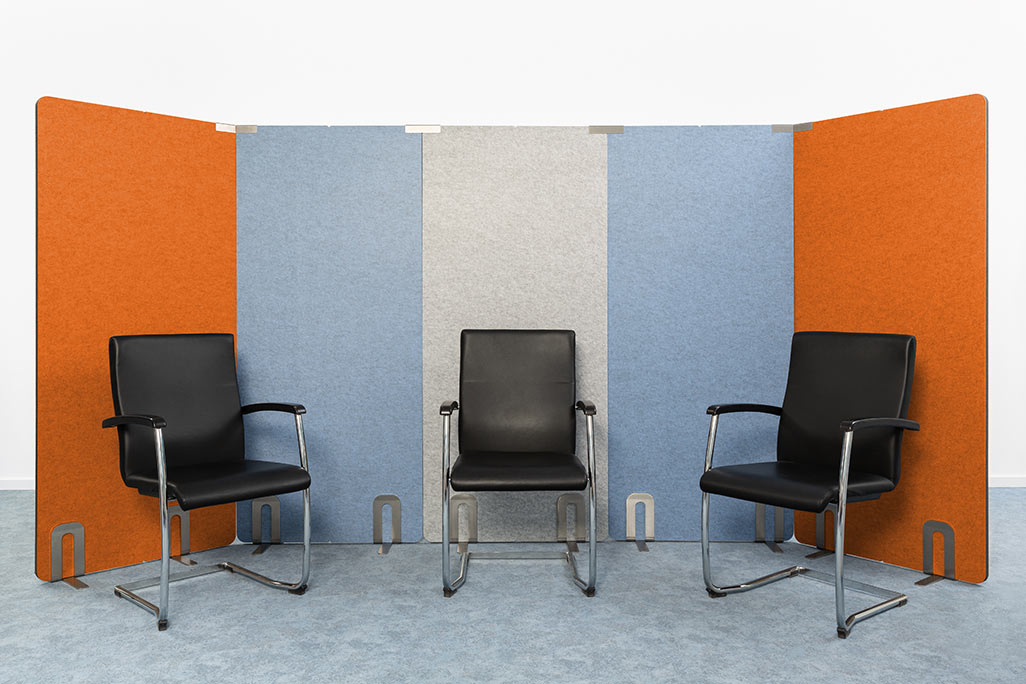 5 partitions from soniflex arranged next to each other in front of a white wall as a U. Several chairs next to each other
